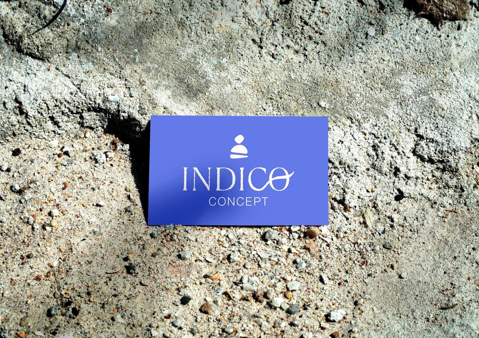 Tarjeta de visita azul iris apoyada en una roca